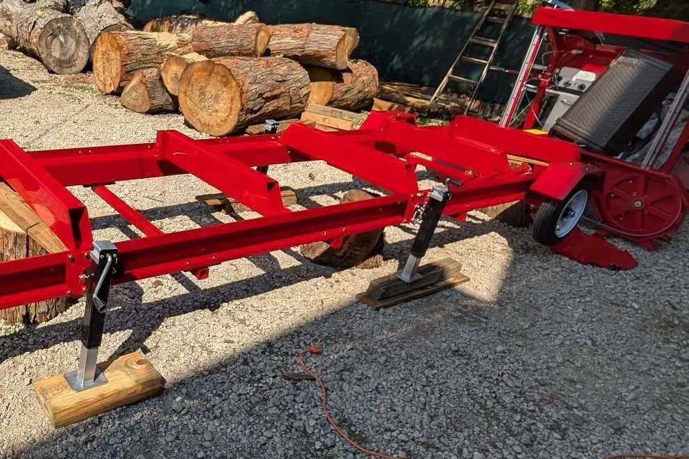 The portable sawmill set up on its trailer frame, with hardwood logs stacked behind it.